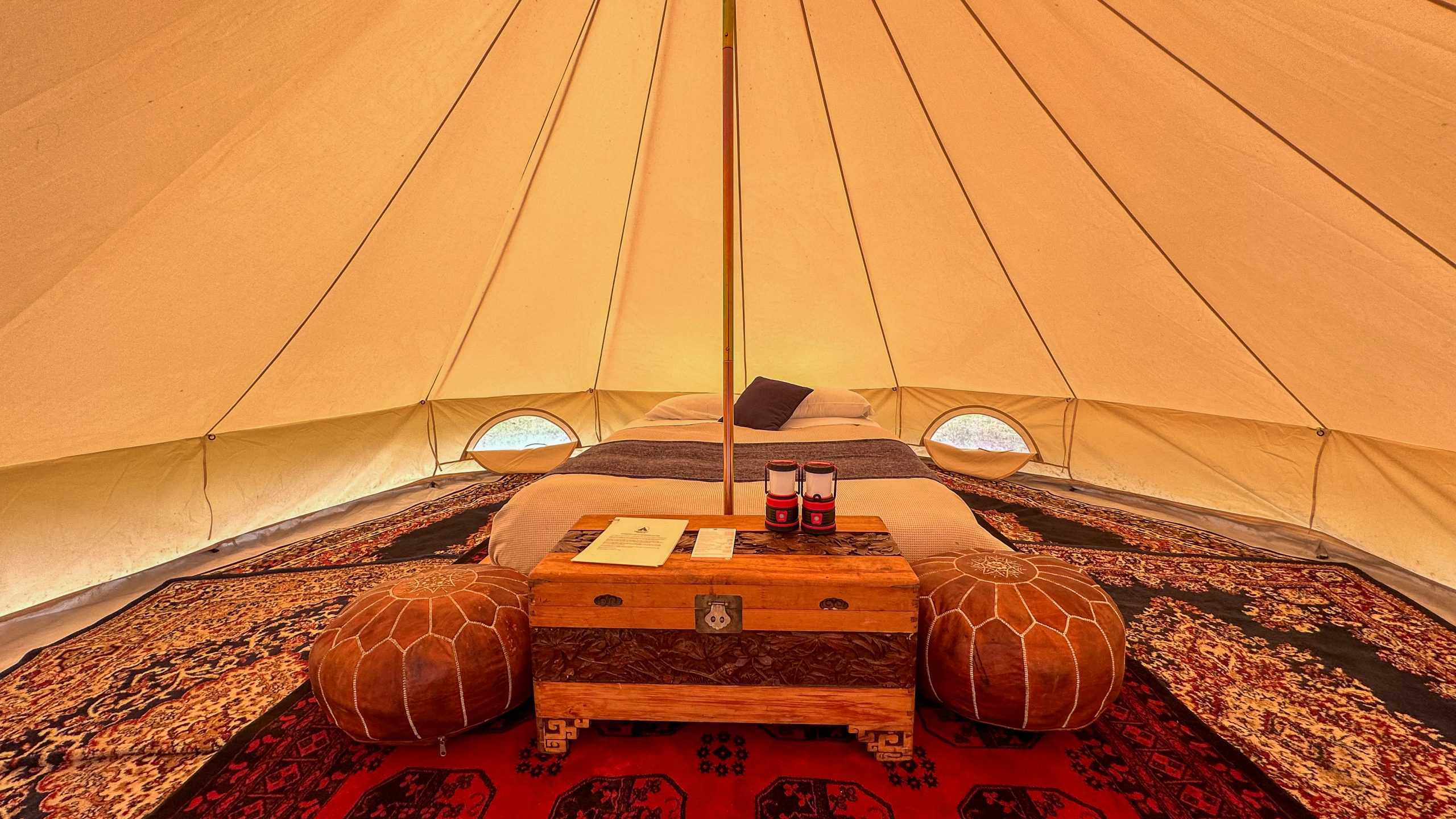 Inside a Glamping Tent: Interior of a glamping tent featuring a queen bed with fresh linens, lanterns, and wooden storage.

