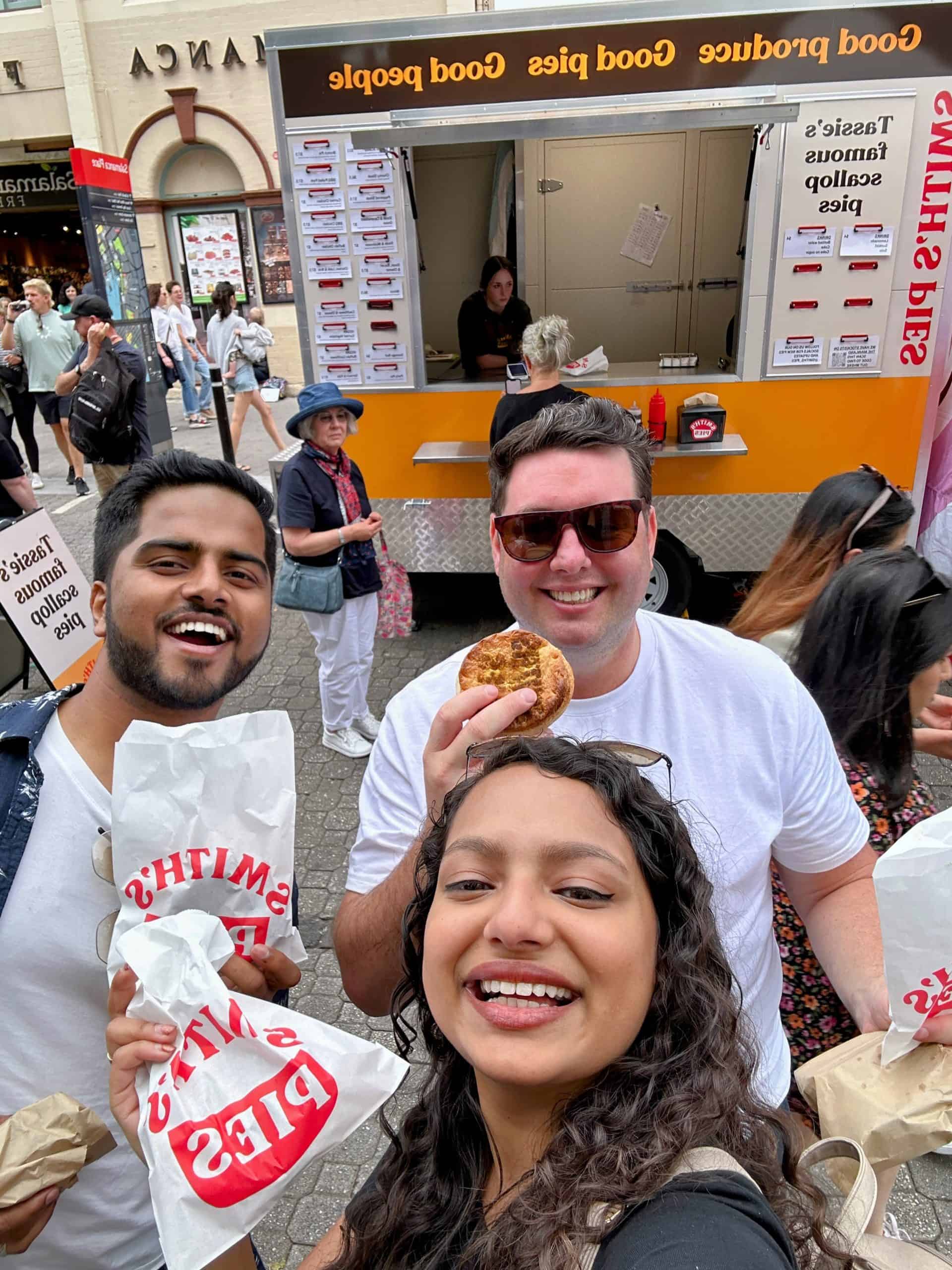 Three people smiling while having food in the Salamanca Market!