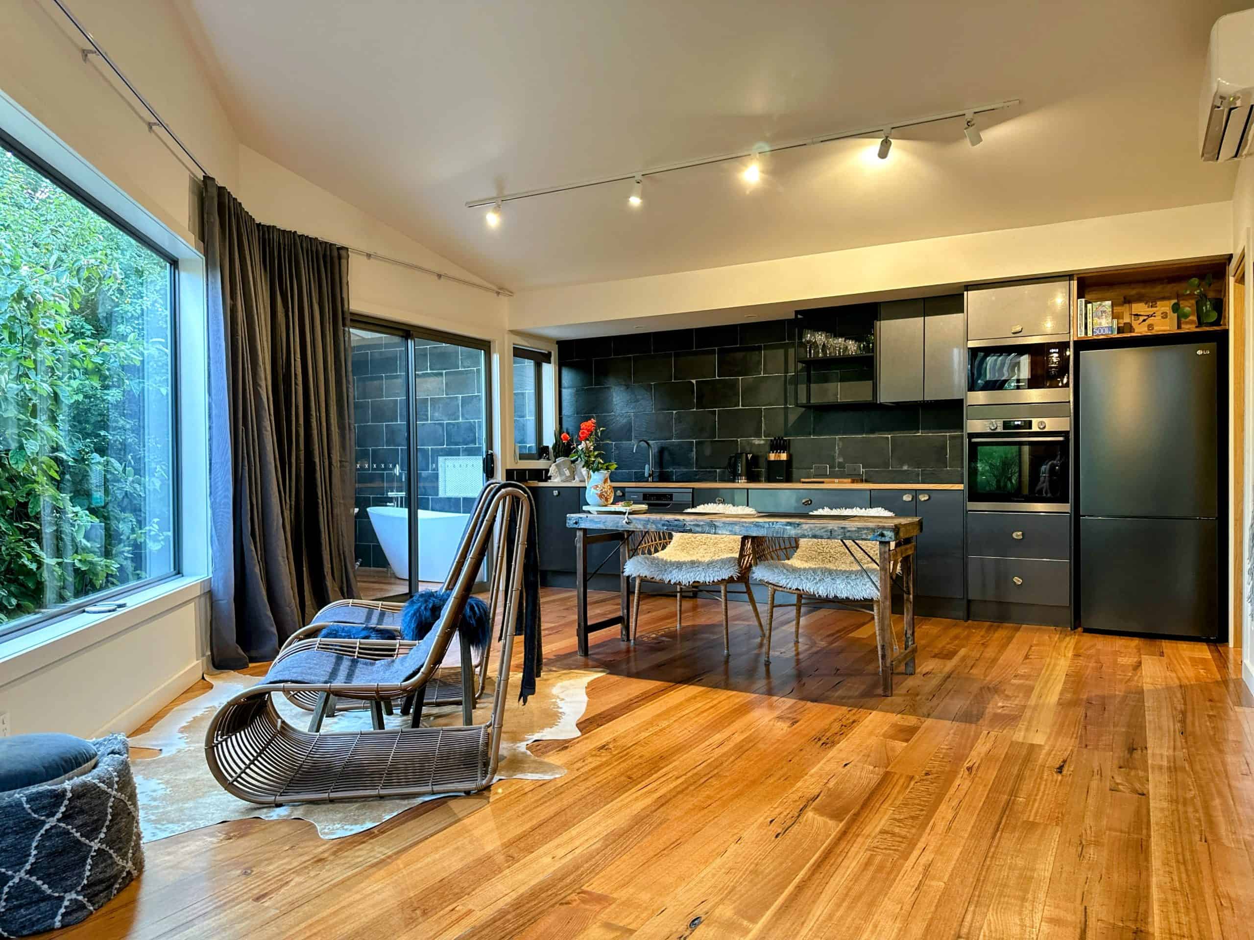 The Zoo Treehouse Living Room & Outdoor Tub: A stylishly furnished living space with a cozy couch and a glimpse of an outdoor bathtub on a wooden deck.

