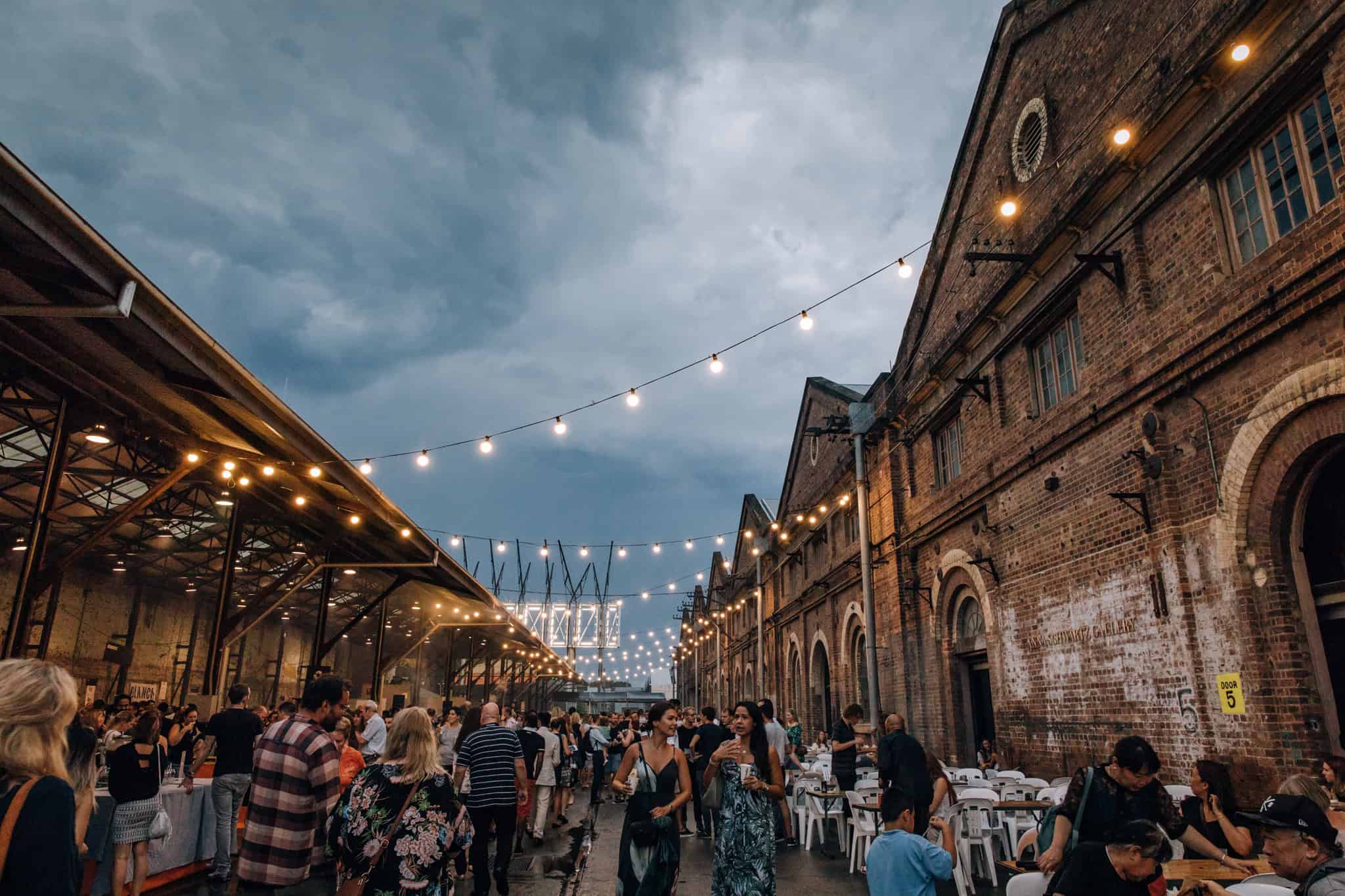  A lively scene from the Carriageworks Night Market at Vivid Sydney, filled with gourmet food, artisan vendors, and an ambient glow of colorful lights.