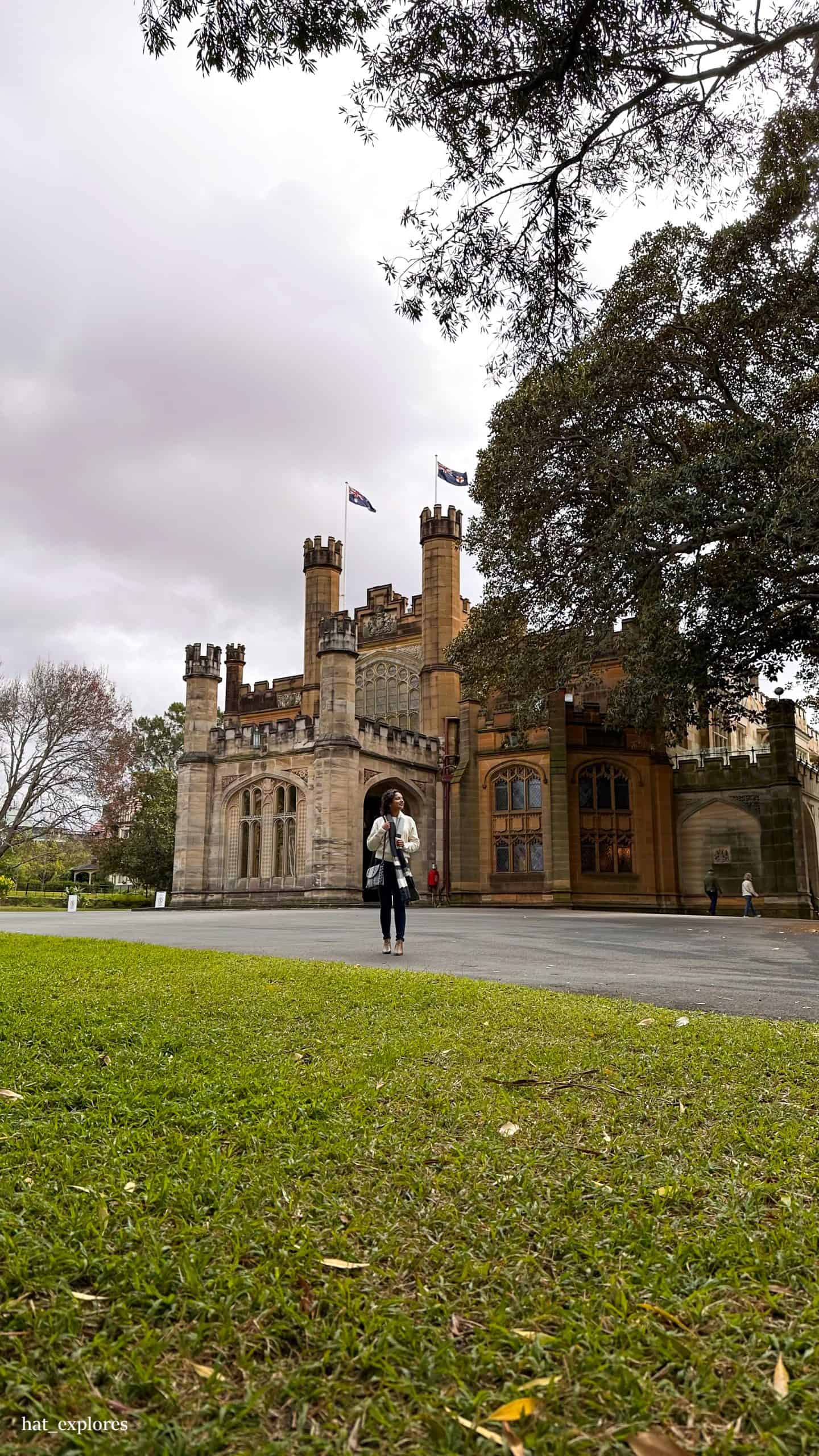 A girl in a white jacket and a sling bag is standing in front of the Government's House