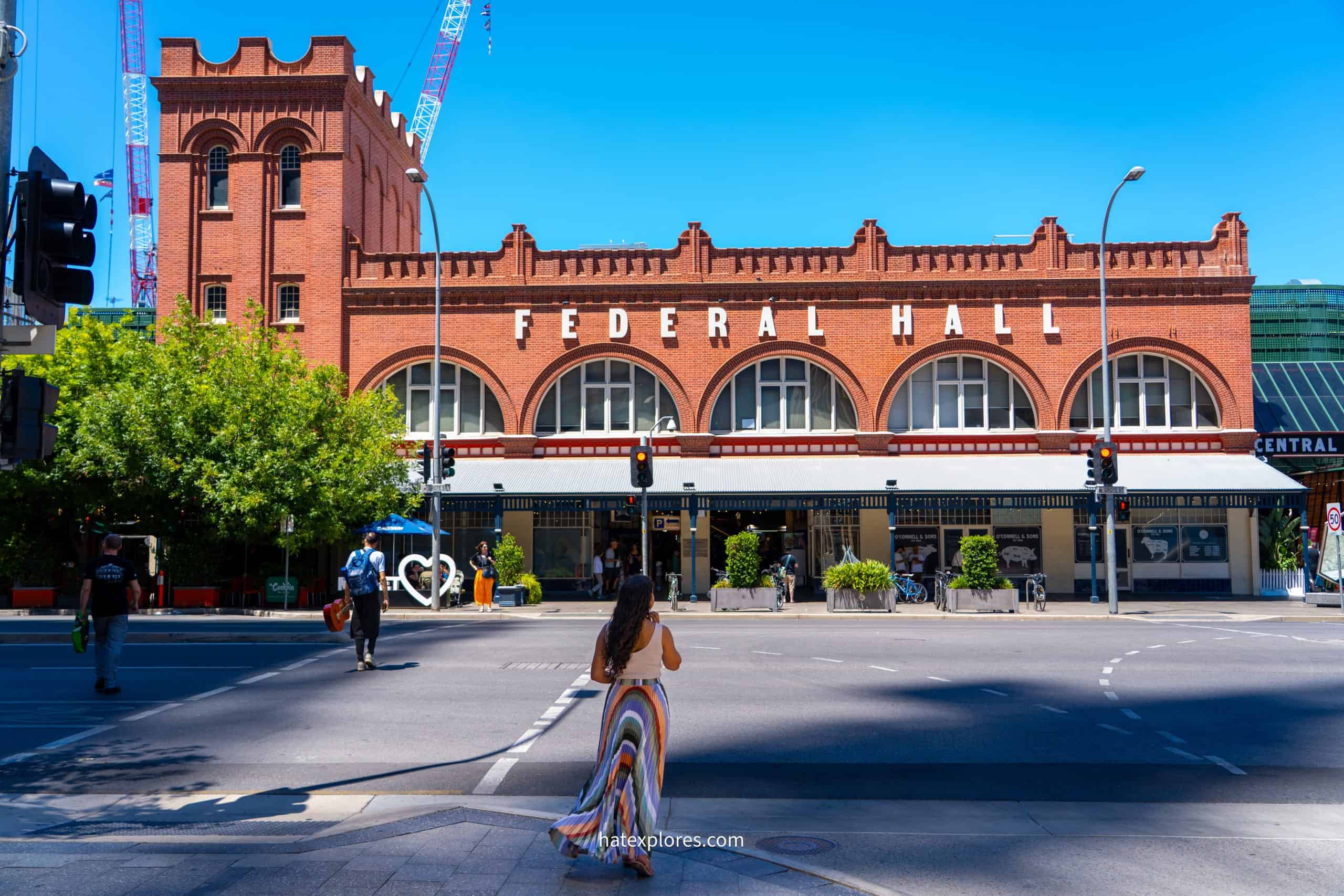 A woman in a colorful skirt crosses a city street towards the red-brick Federal Hall in Adelaide, a great urban stop for day one of a 3 day Adelaide itinerary!