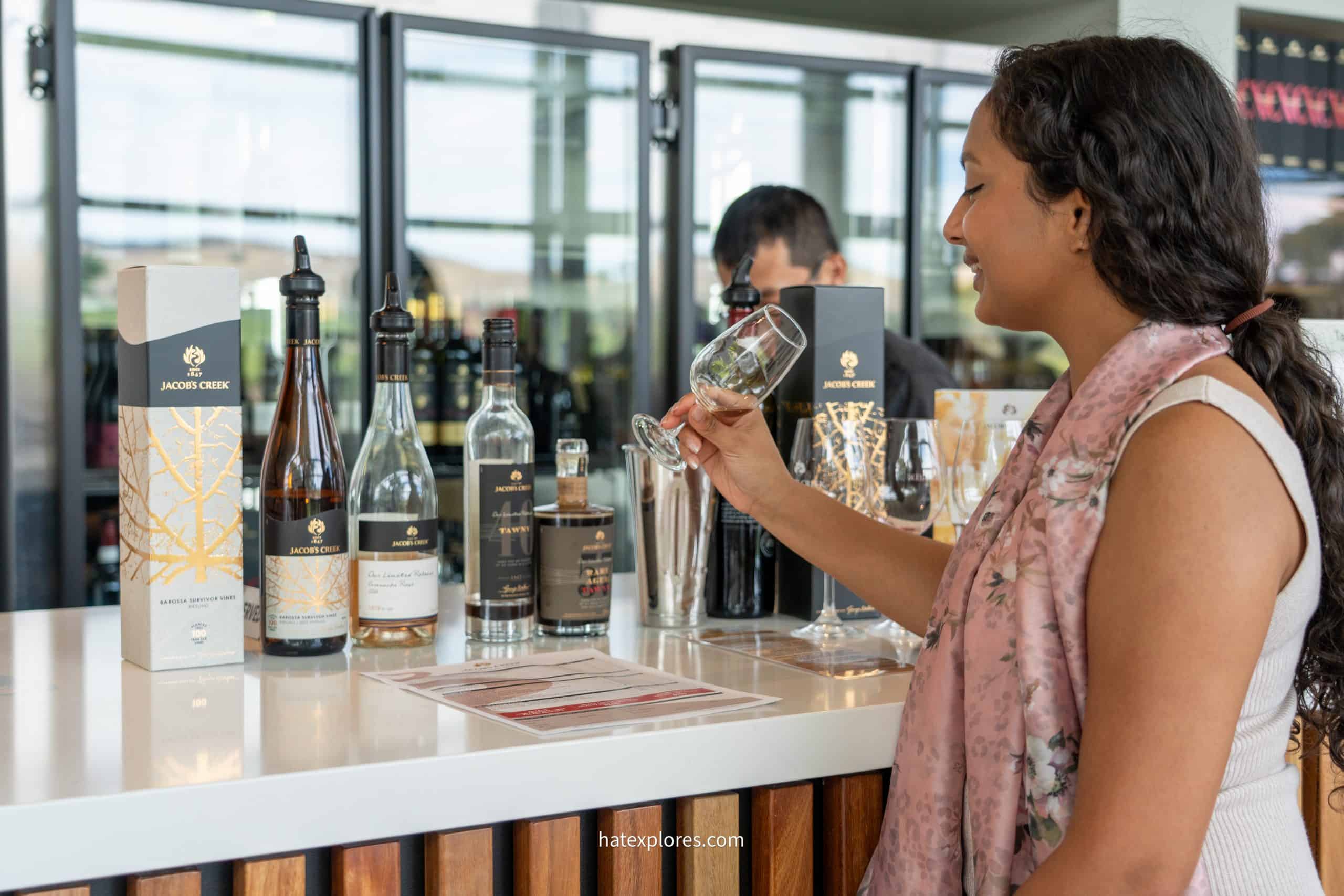 A woman samples wine at Jacob’s Creek winery, surrounded by a tasting menu and premium bottles.