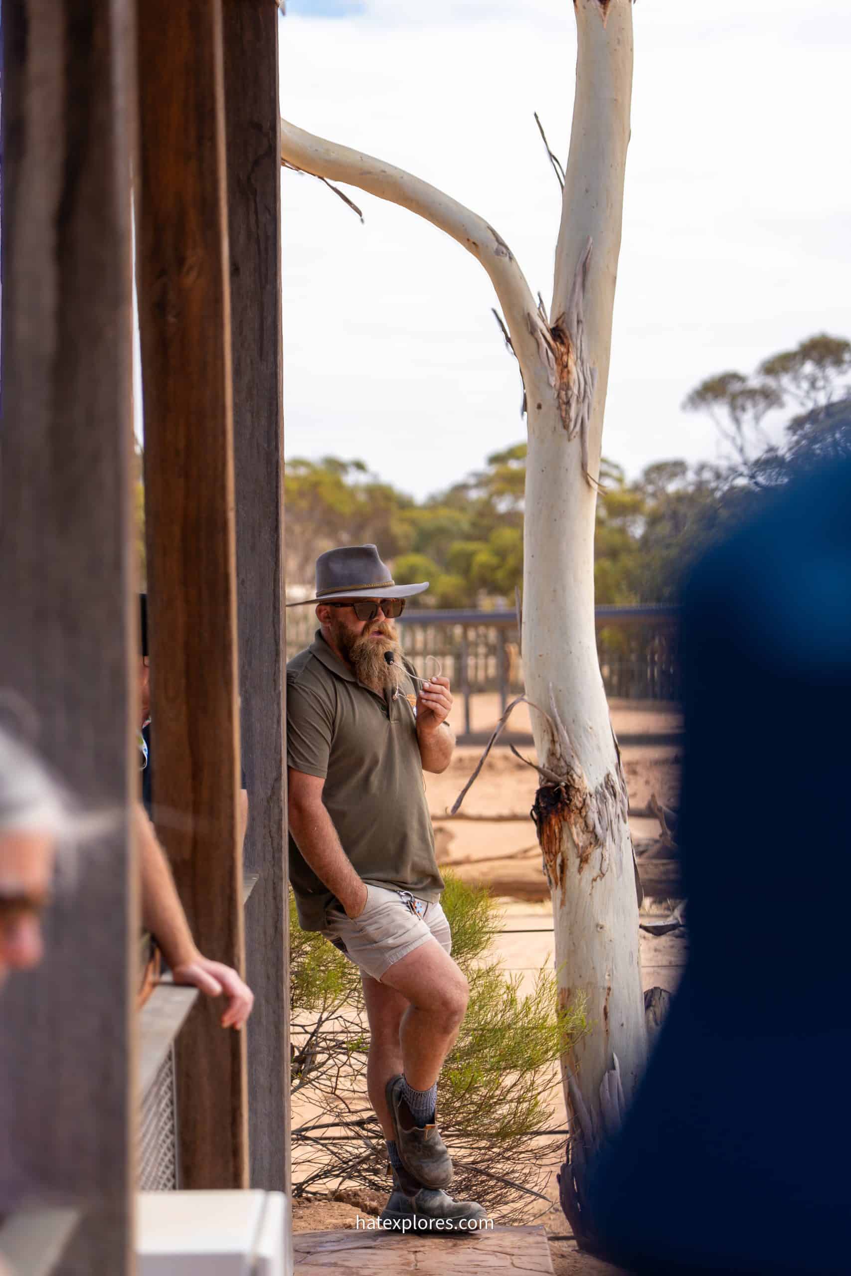 A bearded safari guide in khaki gear and a wide-brim hat leans against a post while giving a talk at Monarto Safari Park.