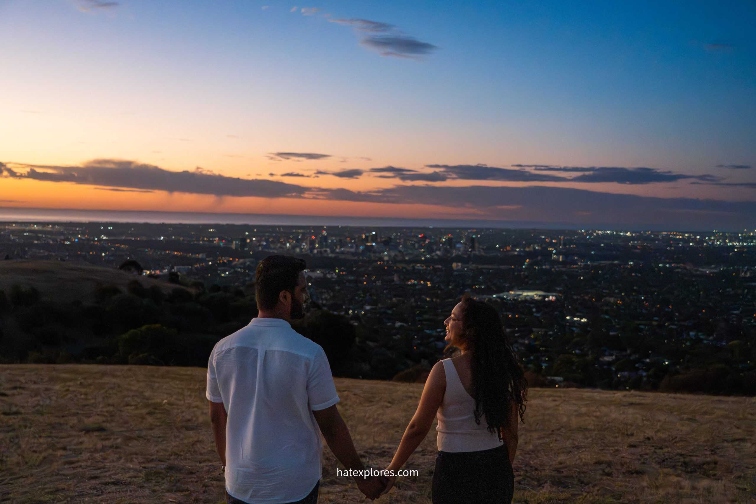 A couple holds hands while overlooking the city of Adelaide at sunset from Mount Osmond, a romantic highlight for any 3 day Adelaide itinerary