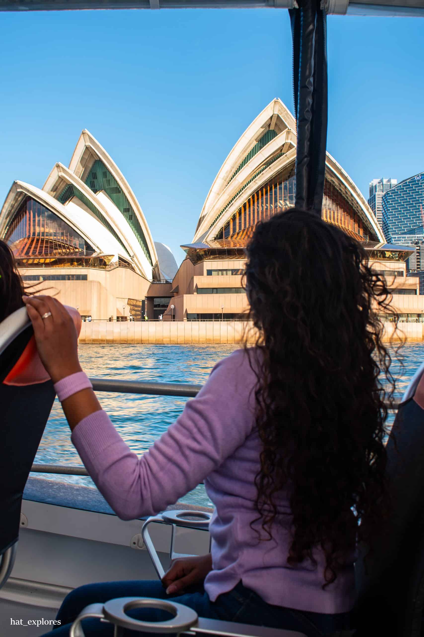 A girl sitting inside a cruise and watching over the Opera House.