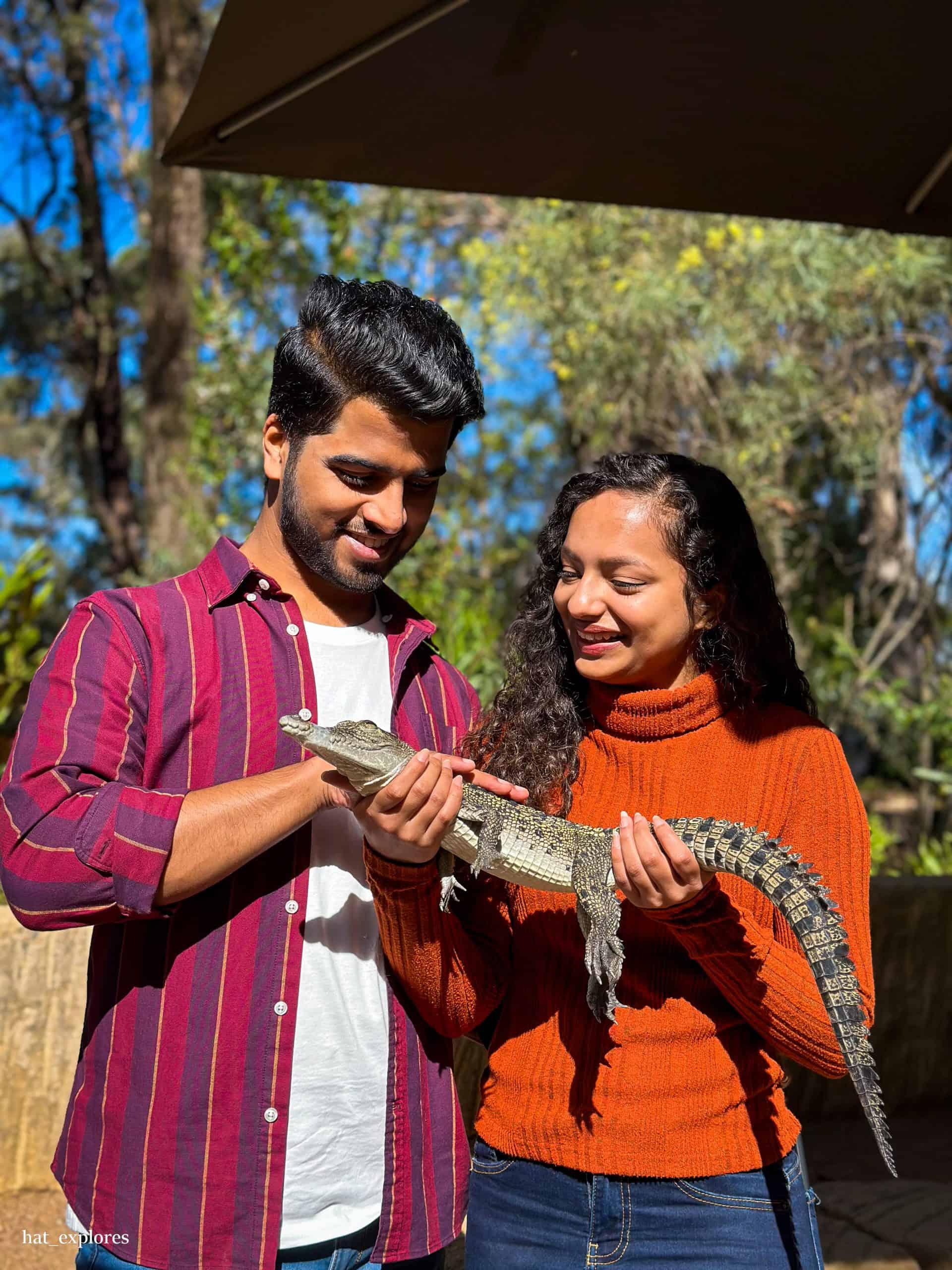 A smiling couple gently holds a baby crocodile at the Australian Reptile Zoo in Wollondilly, offering a fun and educational wildlife experience ideal for day trips from Sydney by car.