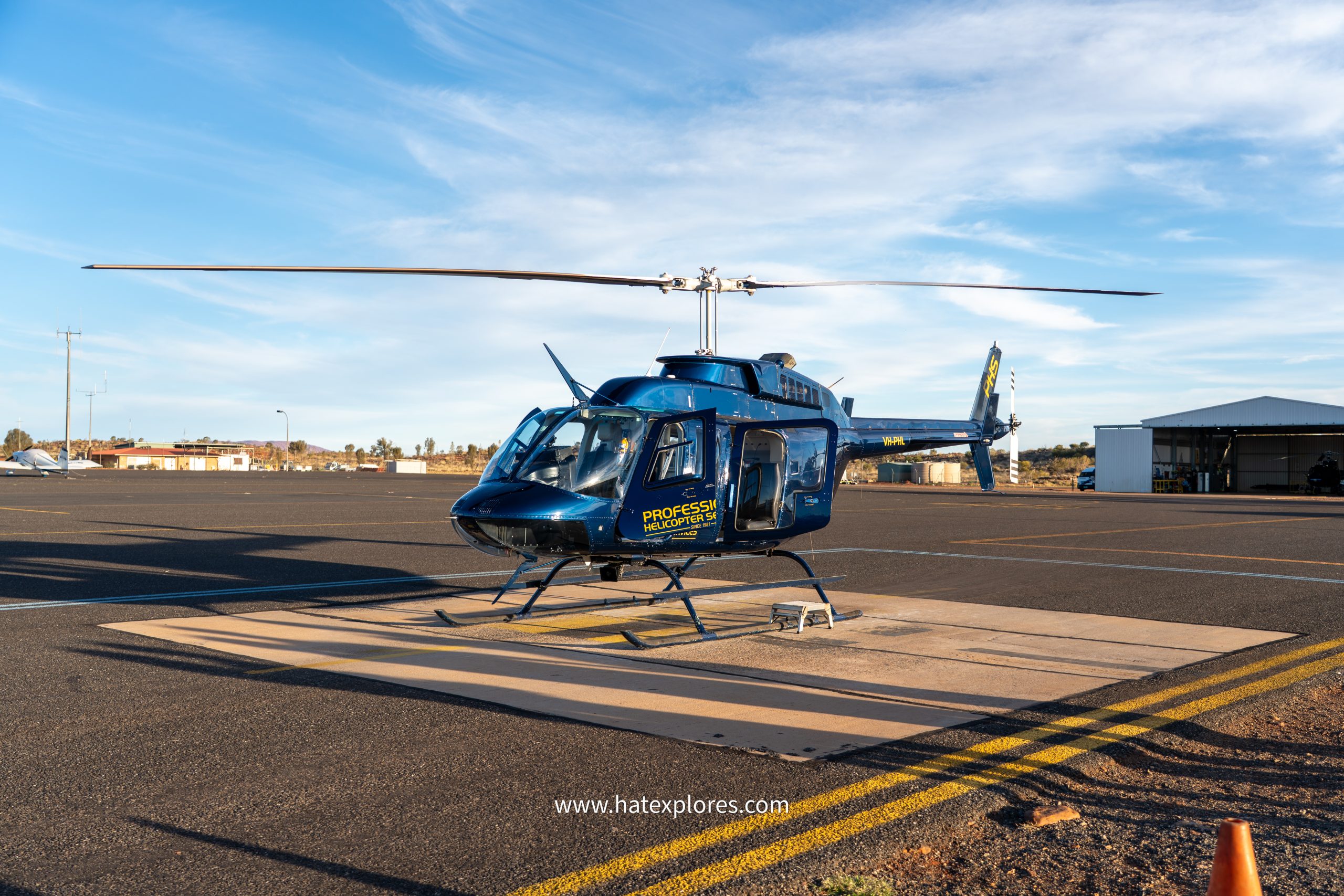 A blue helicopter from Professional Helicopter Services parked on a tarmac under clear skies at the start of a scenic flight, part of one of the best Uluru tour experiences for aerial views of the iconic Australian outback.