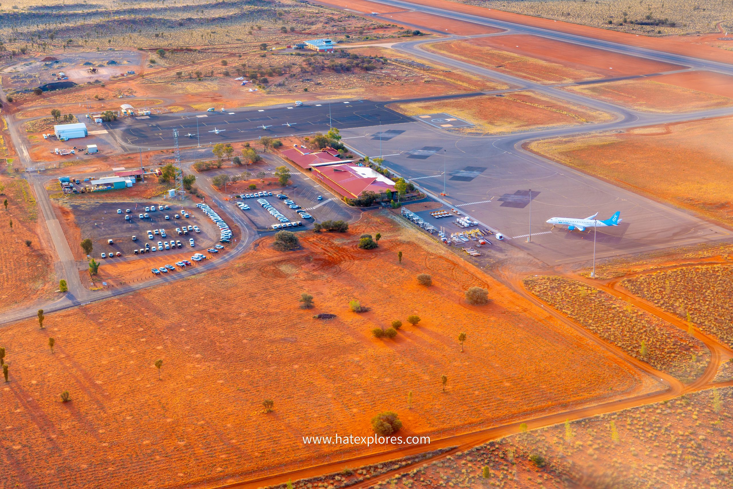Aerial view of Ayers Rock Airport surrounded by vivid red desert landscape, with a tour plane on the tarmac.